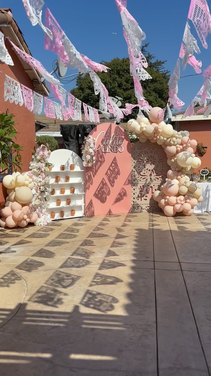 14 Mexican Decor Ideas for Every Room 8 Pink and white papel picado banners hanging over an outdoor patio with balloon decorations.