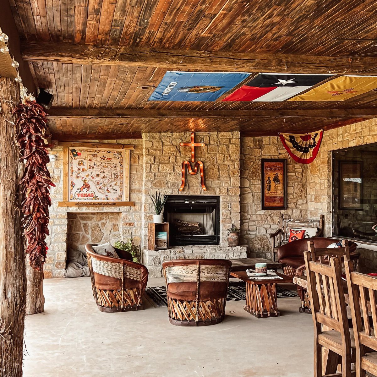 14 Mexican Decor Ideas for Every Room 5 Rustic wooden furniture and leather armchairs arranged in a stone living room with a wooden ceiling.