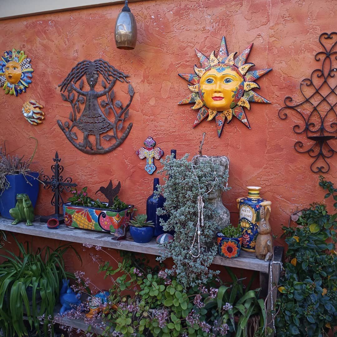 14 Mexican Decor Ideas for Every Room 13 Mexican-style wall decorations including sun masks and metal art on a terracotta wall with potted plants.