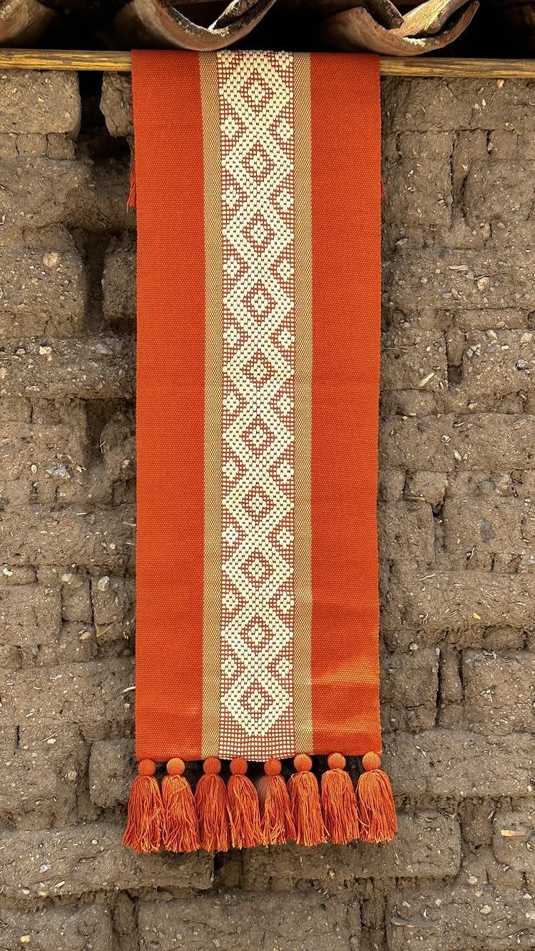 14 Mexican Decor Ideas for Every Room 7 An orange woven textile runner with cream geometric patterns hanging against an adobe brick wall.