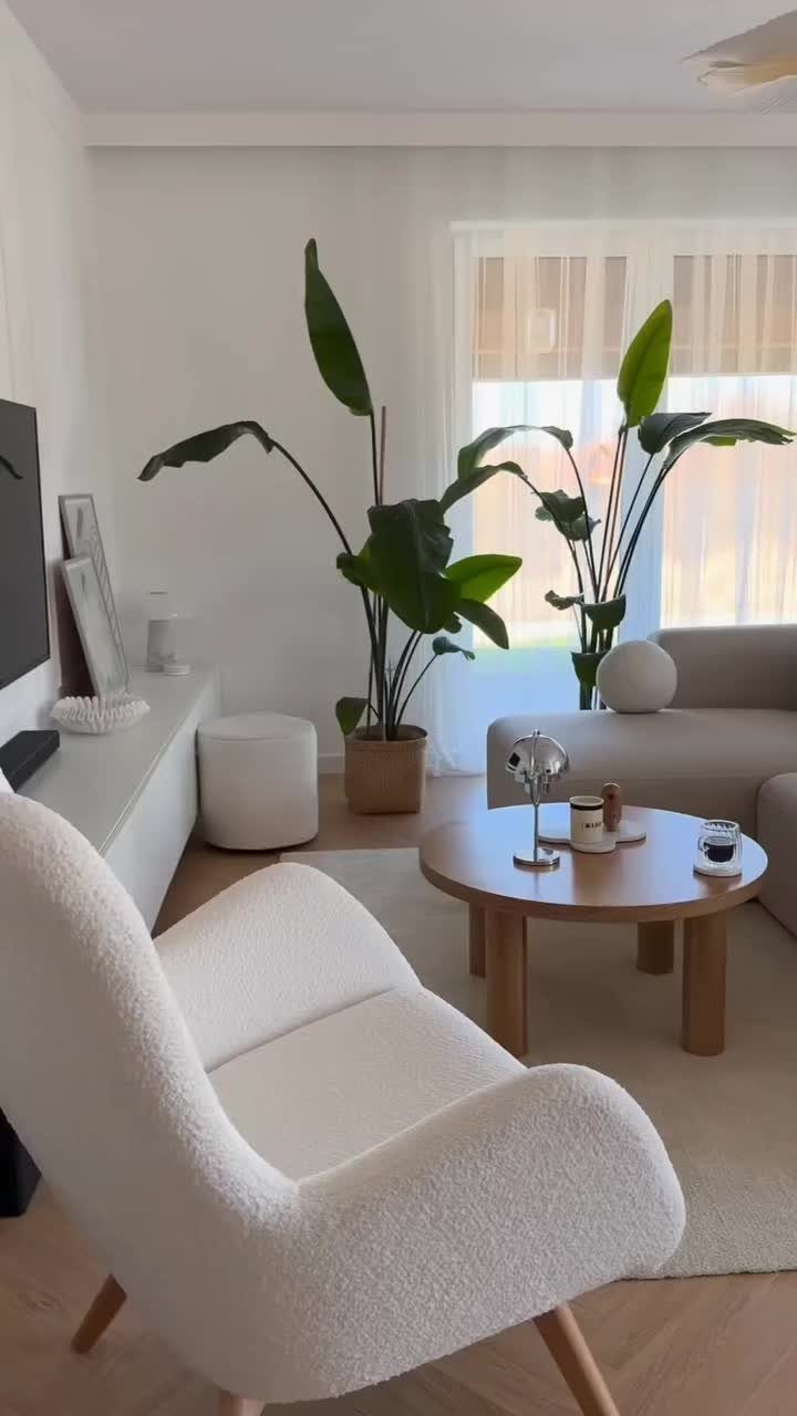 White bouclé armchair and wooden coffee table in a bright, minimalist living room with greenery.