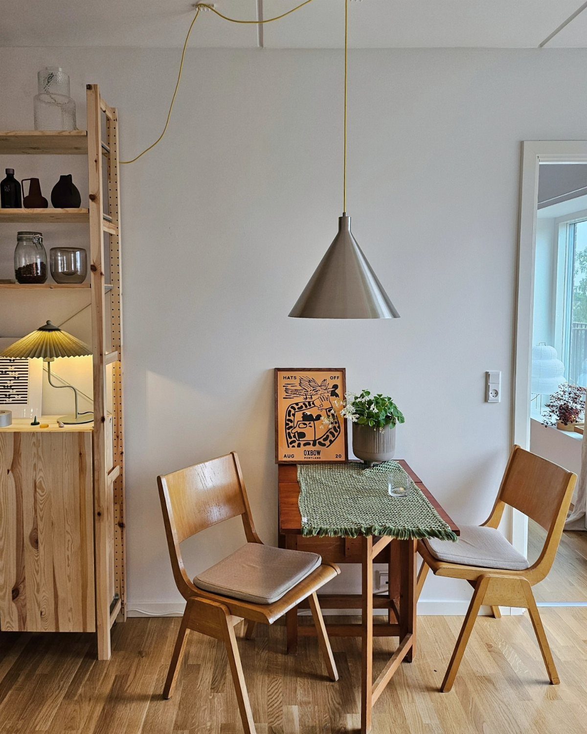 A small wooden dining set with a green runner and potted plant against a white wall.