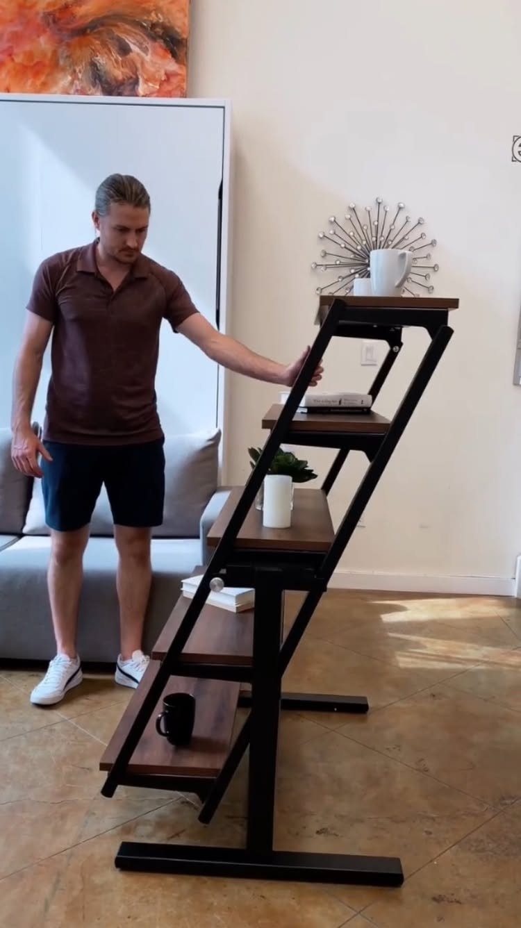A man stands beside a tall, multi-tiered wooden shelving unit in a living room.