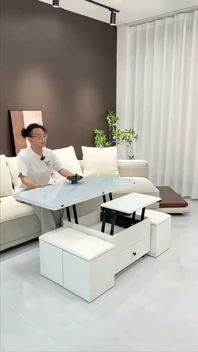 A person sits by a white multifunctional coffee table with built-in storage and stools.