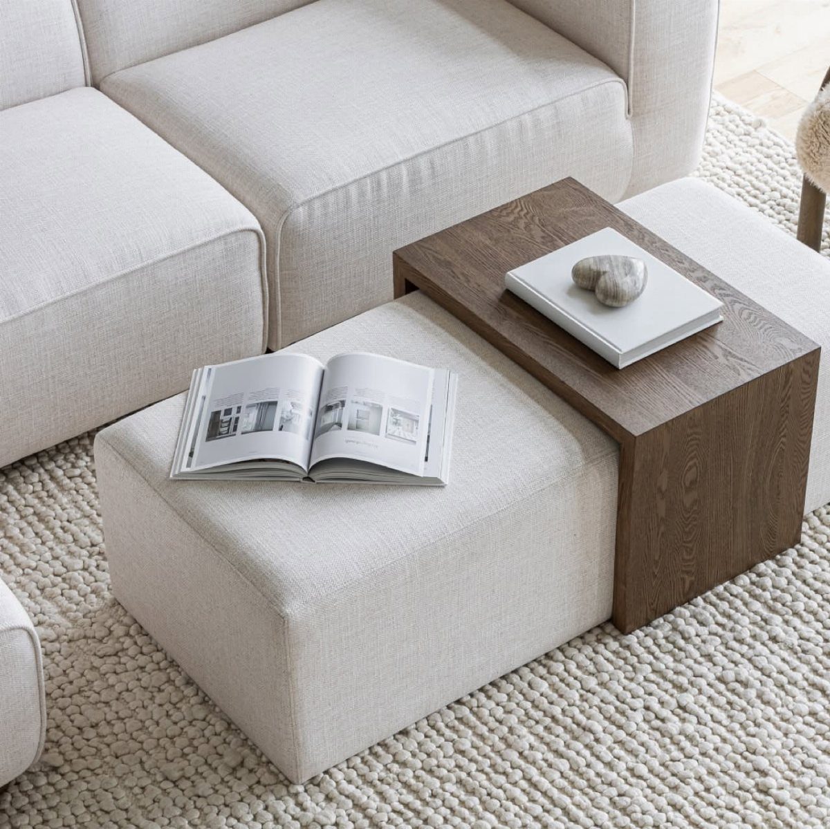 A beige fabric ottoman used as a coffee table with a wooden tray and book.