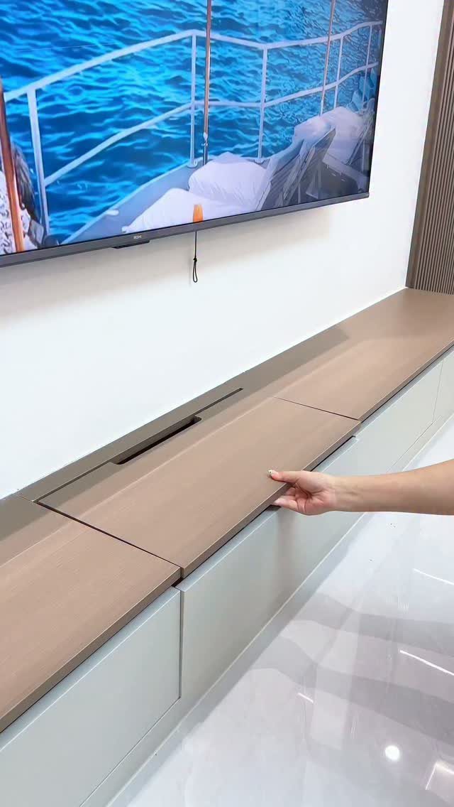 A hand opens a wooden drawer in a modern white media console under a television.