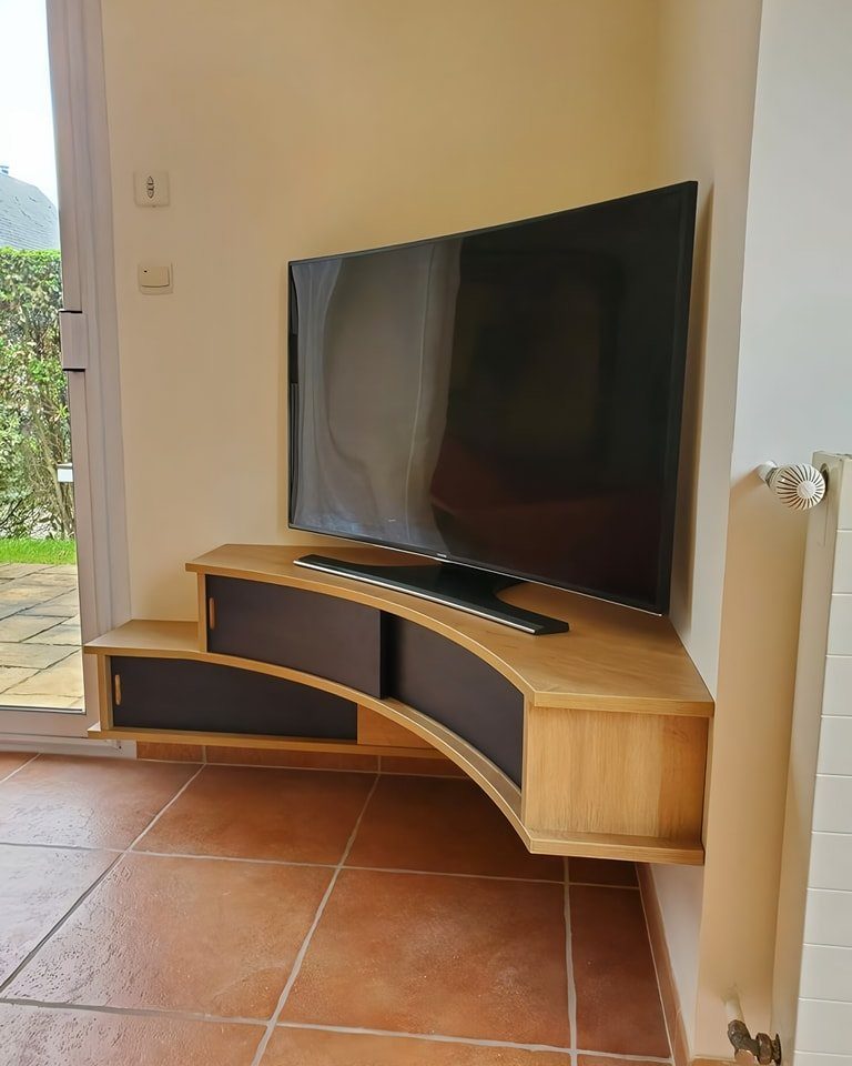 A large television resting on a curved wooden floating corner entertainment unit.