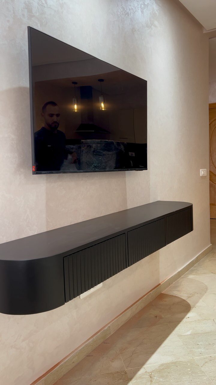 Black floating media console mounted on a beige wall below a television.