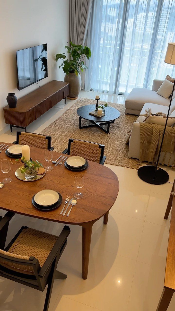 Modern living room with a wall-mounted TV, wooden console, beige sofa, and large windows.