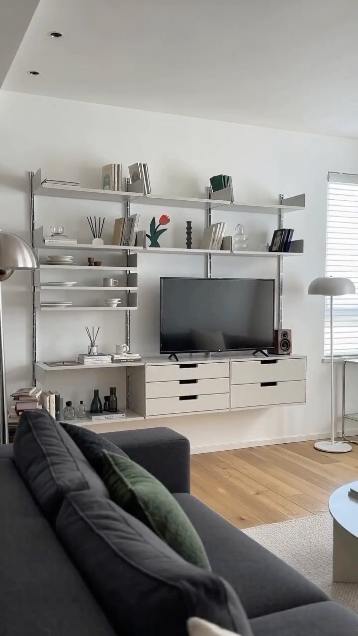 White floating shelves with books and decor mounted above a television and drawers.