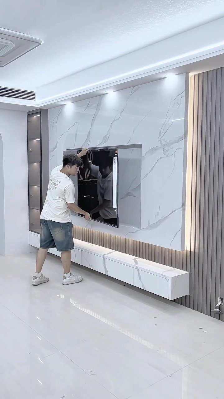 A man installing a television into a recessed niche within a marble-patterned accent wall.