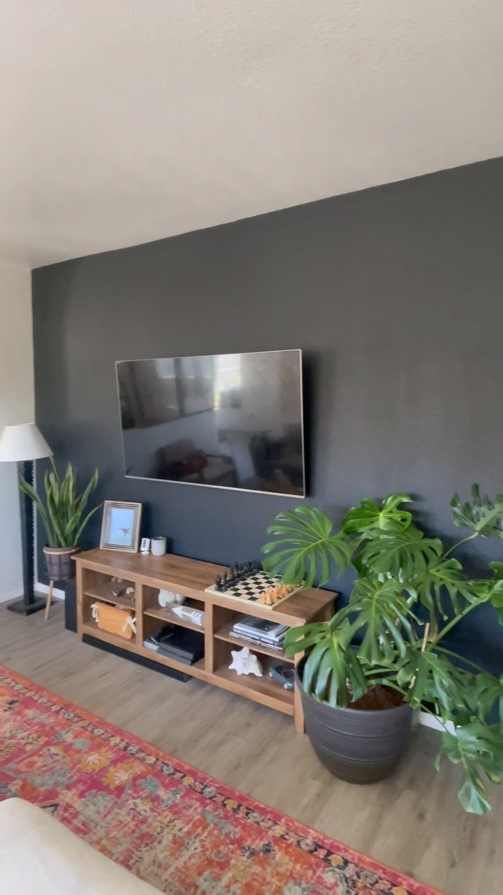 A television mounted on a dark grey accent wall above a wooden media console.