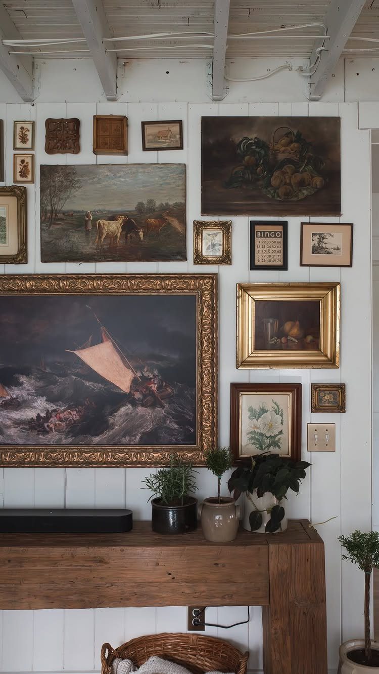 Various framed landscape and still life paintings arranged in a gallery wall on a white paneled wall.